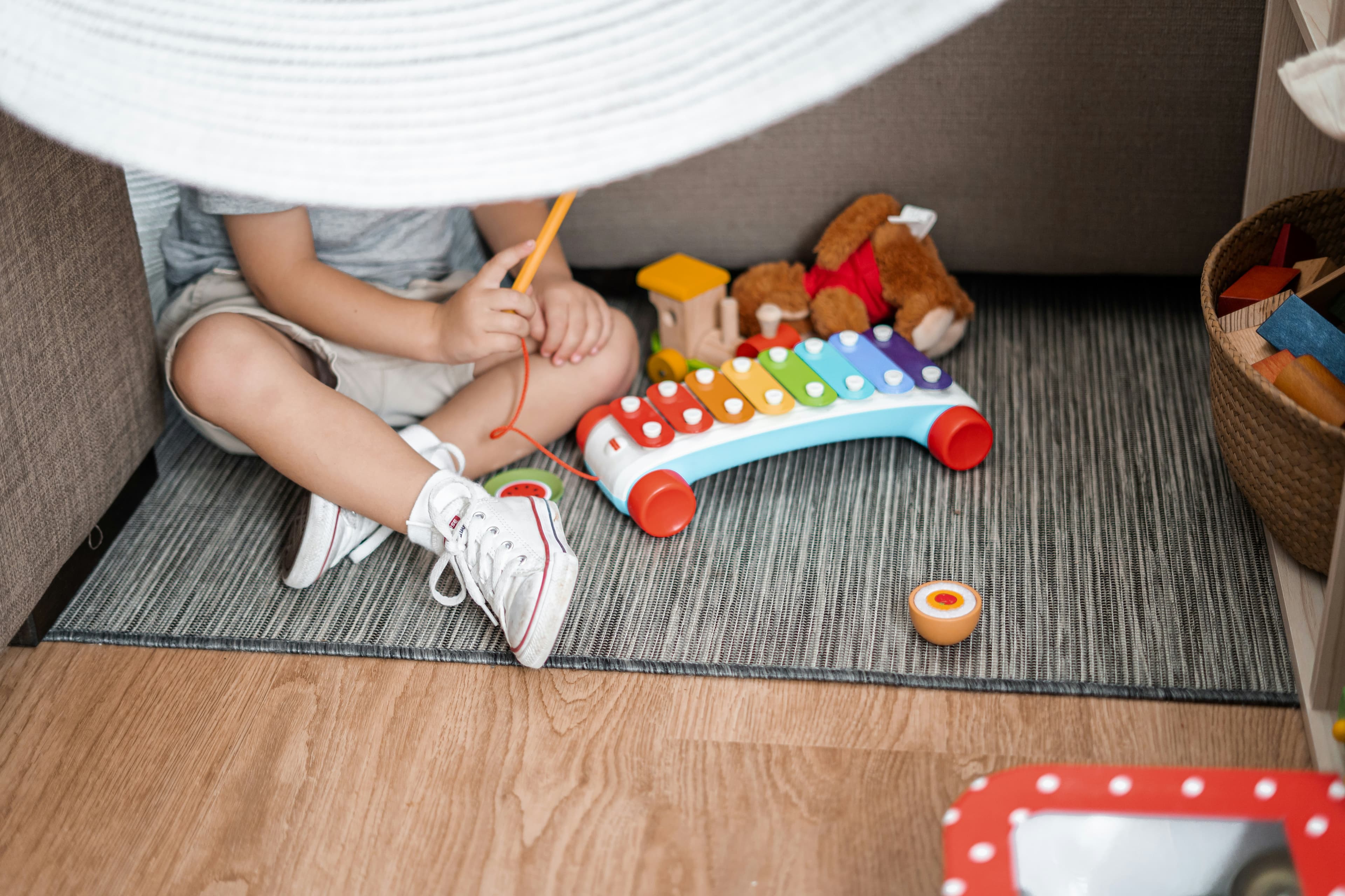 Un enfant est assis sous une cabane de couverture, avec un xylophone jouet à côté de lui.